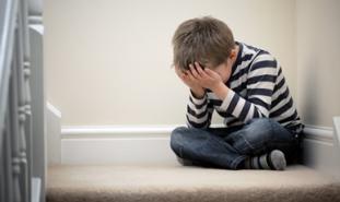 little boy sitting on the floor covering his face